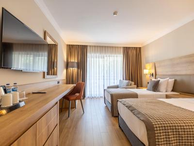 Helles Hotelzimmer mit zwei Betten, Holzmöbeln und großem Fenster mit Vorhängen.