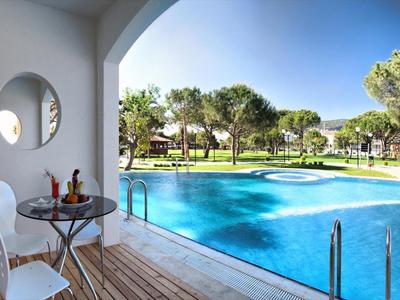 Terrasse mit weißem Stuhl, Tisch, Pool mit blauem Wasser und grünem Park im Hintergrund.