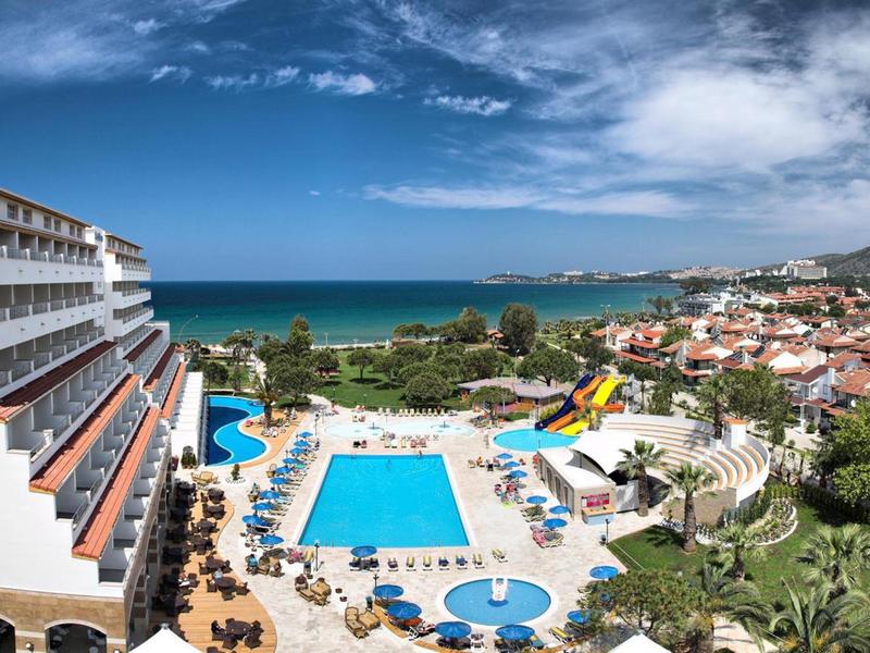 Vista di un hotel con più piscine, lettini prendisole e il mare sullo sfondo.