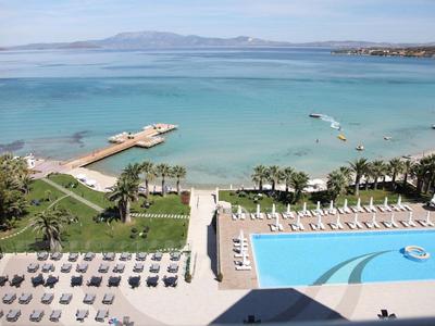 Blick auf einen Strand mit klarem Wasser, Schwimmbad, Liegen und einem grünen Garten.