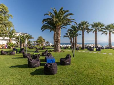Green lawn with bean bags and palm trees in front of a hotel by the sea on a sunny day.