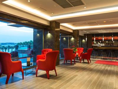 Modern hotel bar with red armchairs and a sea view at dusk.