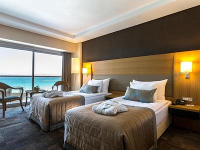 Hotel room with two beds, sea view, and seating area by window in daylight.