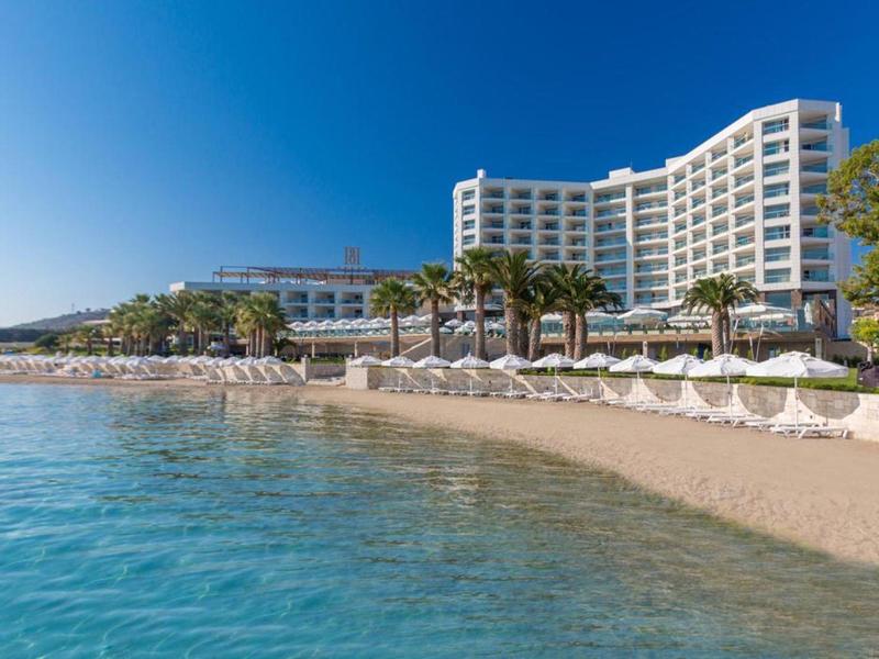 Hotel na písečné pláži s slunečníky a průzračně modrou vodou.