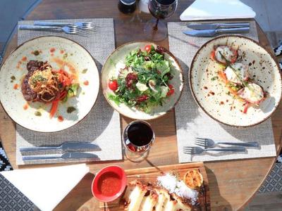 Mesa de restaurante con tres platos gourmet, ensalada y bebidas servidos en vajilla elegante.