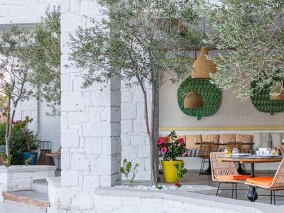 Patio moderno con paredes de piedra blanca, plantas verdes y asientos variados en la cafetería.