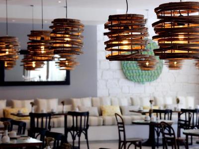 Acogedora zona de salón de hotel con lámparas colgantes de madera y sillas negras.