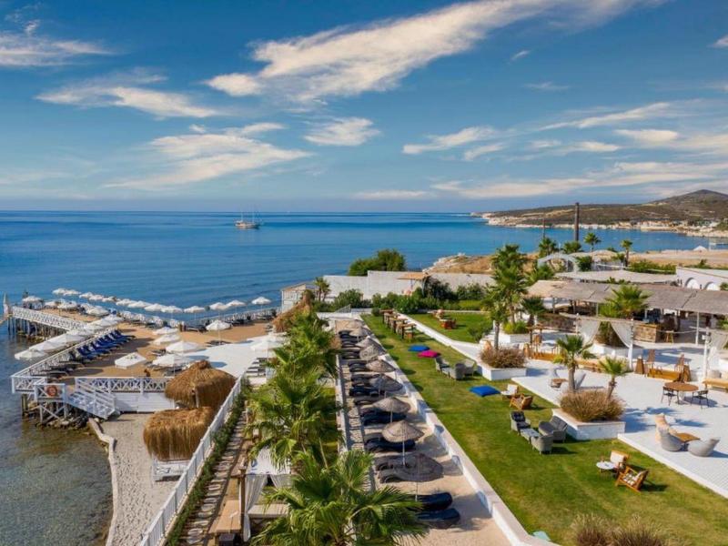 Costa con instalaciones de hotel, tumbonas y sombrillas junto al mar bajo cielo azul.
