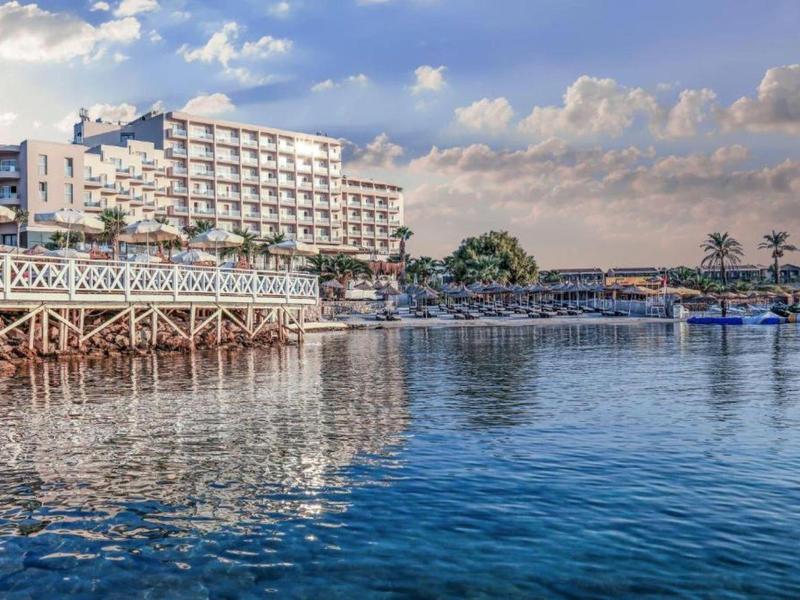 Gran edificio de hotel junto a agua tranquila bajo cielo azul con nubes.