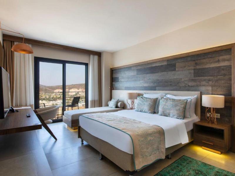 Habitación de hotel moderna con cama doble, detalles en madera y vistas a un paisaje montañoso a través de grandes ventanas.