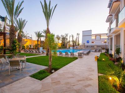 Moderner Hotelpoolbereich mit Liegestühlen, Palmen und beleuchteten Wegen bei Abenddämmerung.