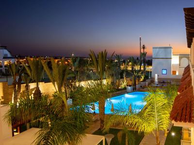 Beleuchteter Poolbereich umgeben von Palmen bei Sonnenuntergang in einem Hotel.