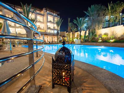 Ein beleuchteter Poolbereich bei Nacht mit dekorativer Laterne und Hotelgebäude im Hintergrund.