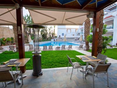 Blick auf einen Hotelpool von einer überdachten Terrasse mit Tischen und Stühlen.