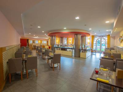 Großer, hell beleuchteter Hotel-Restaurantbereich mit Tischen, Stühlen und Buffetstation.