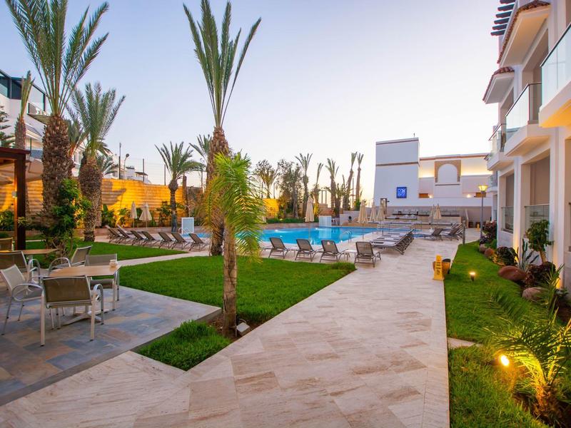 Moderner Außenbereich mit Pool, Palmen, Liegestühlen und Sitzgelegenheiten in einem Wohnkomplex.