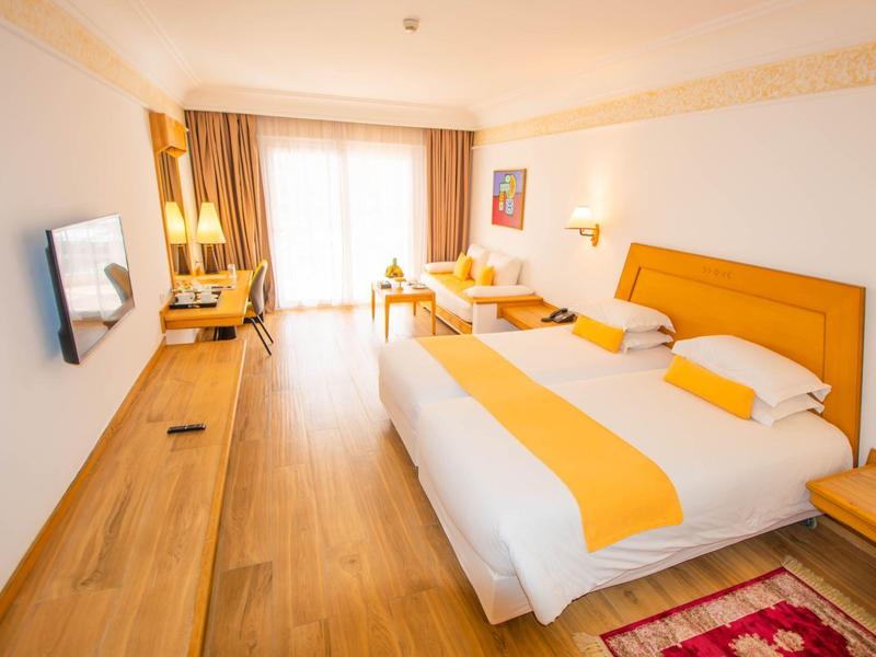 Geräumiges Hotelzimmer mit Doppelbett, Holzmöbeln, hellen Vorhängen und warmem Licht.