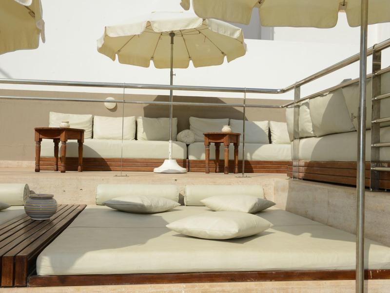 Dachterrasse mit beigen Polstern, weißen Kissen, Holztischen und großen Sonnenschirmen.