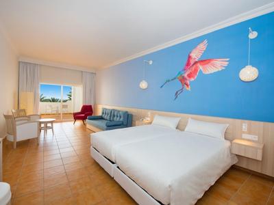 Camera d'hotel con letto grande, parete blu con motivo uccello e zona soggiorno vicino alla finestra.