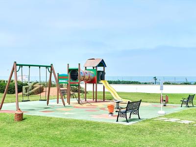 Parco giochi con scivoli, altalene e panchine vicino al mare in una giornata di sole.
