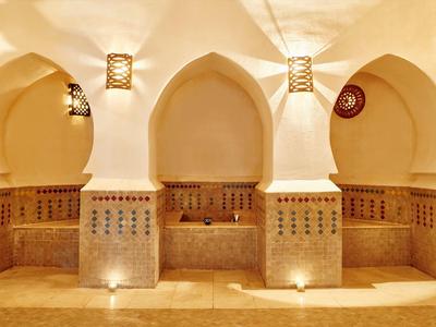 Bagno tradizionale con nicchie ad arco e pareti piastrellate illuminate da luce calda.