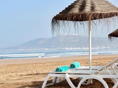 Lettini da spiaggia con asciugamani turchesi sotto ombrelloni di paglia sulla spiaggia sabbiosa.