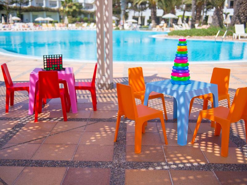 Sedie di plastica colorate e un tavolo con una torre di nastri accanto a una piscina all'aperto.