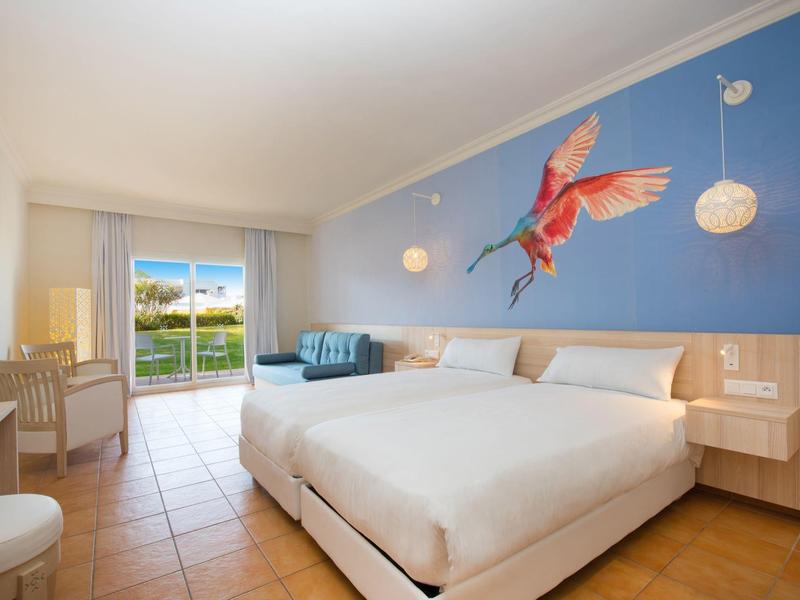 Camera d'hotel luminosa con letto matrimoniale, decorazione murale blu e vista su una terrazza.