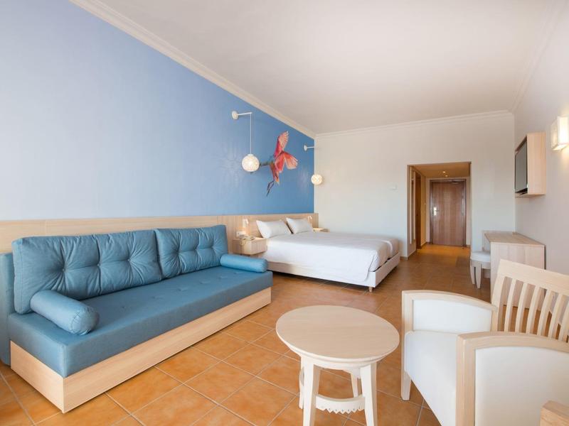Spaziosa camera d'hotel con divano blu, letto matrimoniale e mobili in legno chiaro.