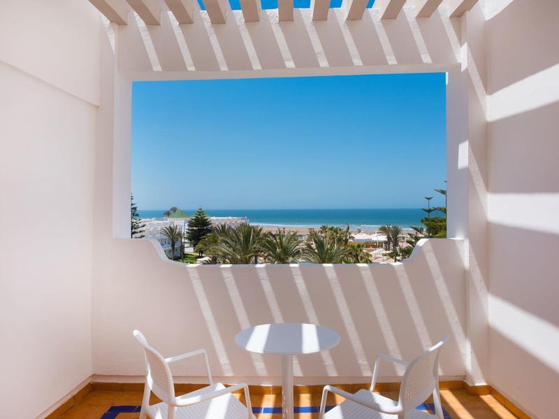 Balcone con tavolo e sedie bianchi con vista sul mare sotto un cielo sereno.