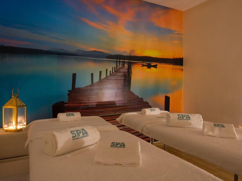 Due lettini da spa con asciugamani bianchi davanti a una parete con foto di un tramonto