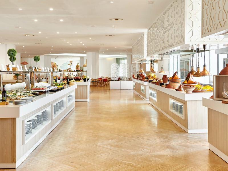 Area colazione luminosa e moderna con tavoli a buffet e varietà di piatti.