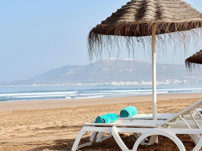 Lettini da spiaggia con asciugamani turchesi sotto ombrelloni di paglia sulla spiaggia sabbiosa.