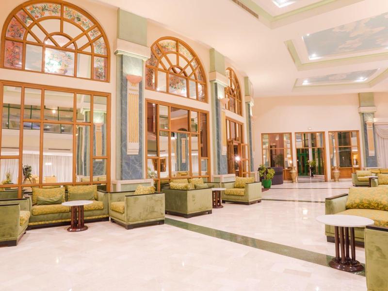 Vaste hall d'hôtel lumineuse avec canapés verts et grandes fenêtres cintrées.