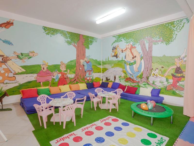 Salle de jeux colorée pour enfants avec peintures murales, canapés vifs, chaises en plastique et tapis de jeu.