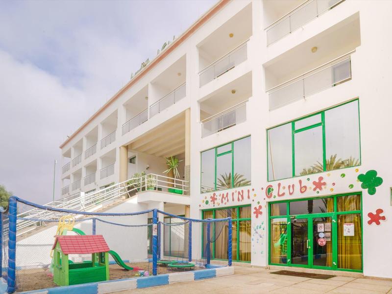 Bâtiment d'hôtel blanc bien éclairé avec aire de jeux et fenêtres vertes.