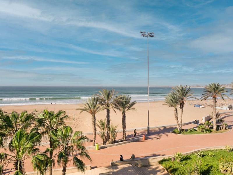 Promenade de plage avec des palmiers et une route, vue sur l'océan sous un ciel bleu.