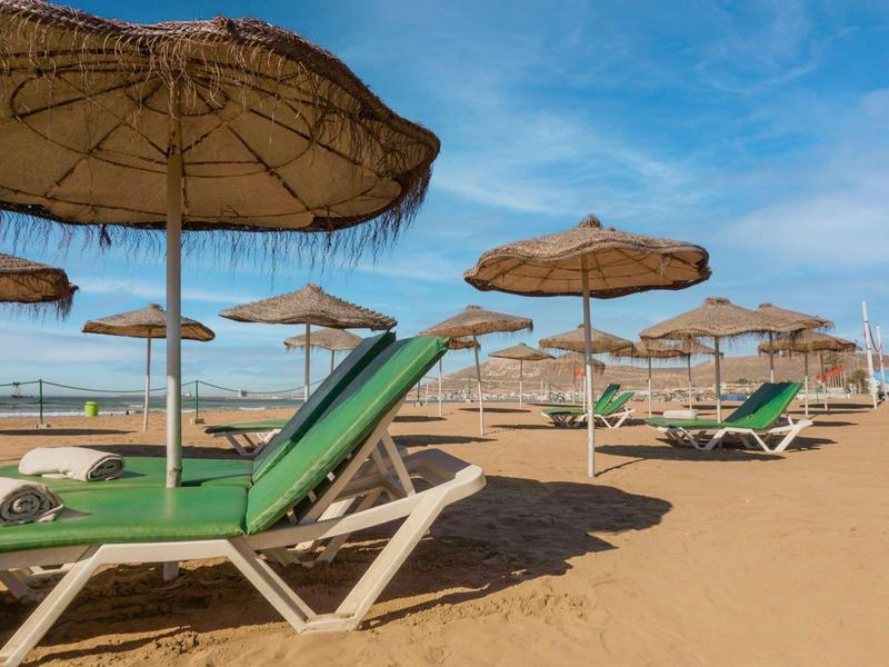 Parasols et chaises longues sur une plage de sable sous un ciel dégagé.