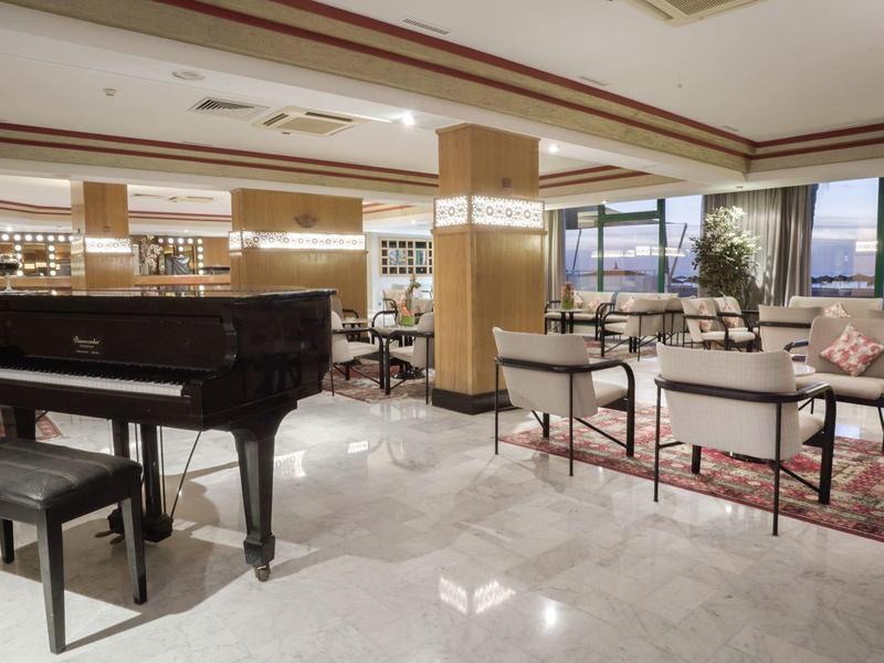 Hall d'hôtel lumineux avec piano, coin salon et grande fenêtre avec vue.