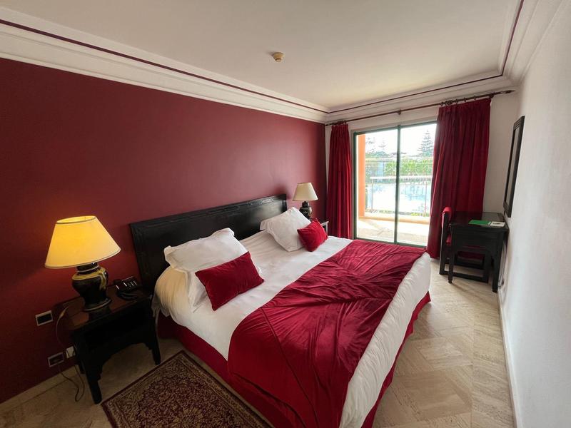 Chambre d'hôtel élégante avec lit double, accents rouges et balcon avec vue extérieure.