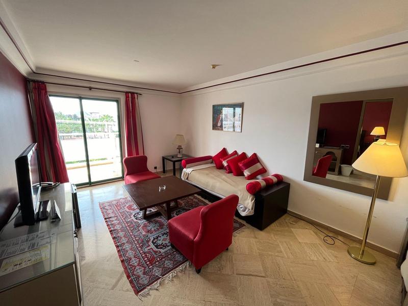 Salon avec fauteuils rouges, canapé, tapis et balcon offrant une vue.