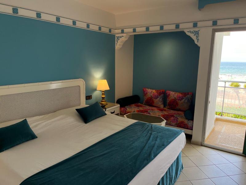Chambre d'hôtel confortable avec grand lit, canapé et balcon avec vue sur la mer.