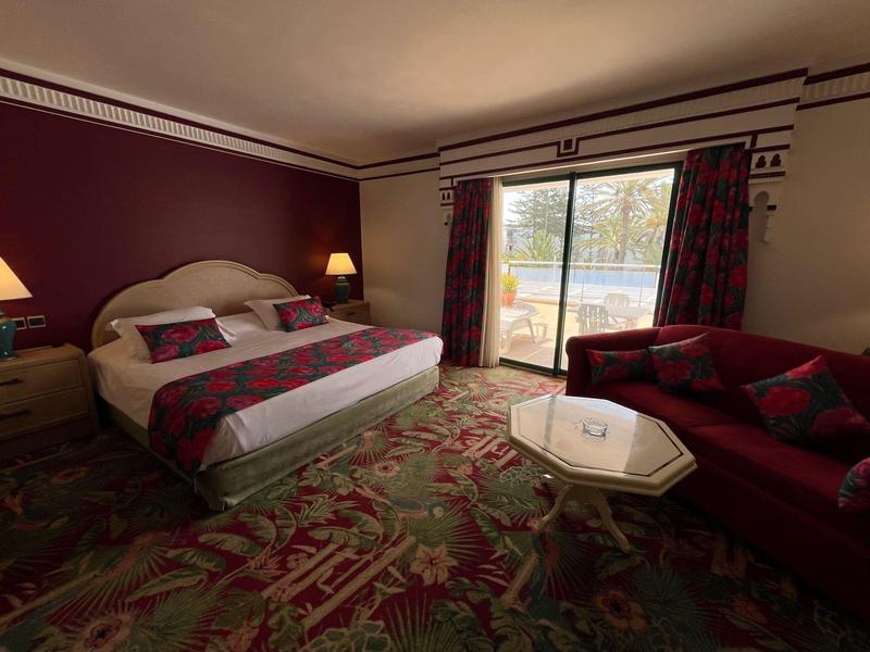 Chambre d'hôtel avec lit double, tapis, canapé, table basse et balcon avec vue extérieure.