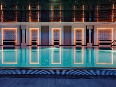 Beleuchteter Pool vor einem modernen Gebäude mit großen Fenstern bei Nacht.