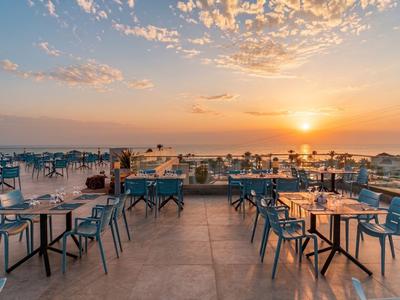 Dachterrasse mit Tischen und Stühlen, Sonnenuntergang über Meer im Hintergrund.