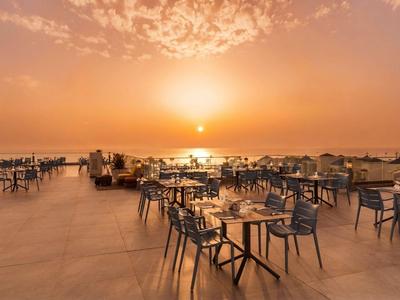 Leerer Terrassenbereich eines Hotels mit Tischen und Stühlen bei Sonnenuntergang.