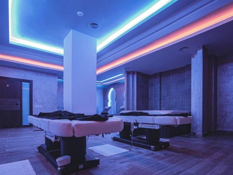 Moderne Massageräume mit zwei Liegen, blau-rote LED-Deckenbeleuchtung und grauen Wänden.