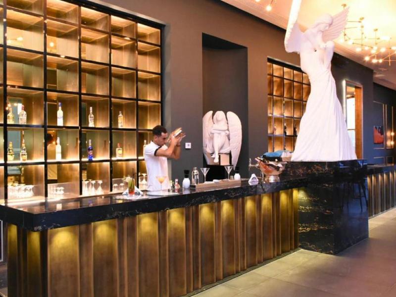 Moderner Barbereich mit beleuchtetem Holzregal, langer Theke und großer weißer Statue.