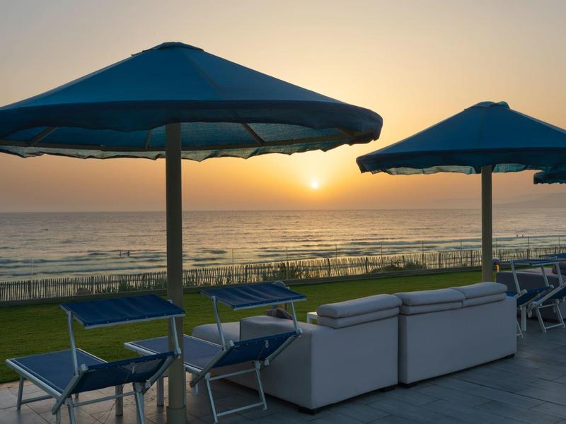 Strand mit blauen Sonnenschirmen, Stühlen und Couch bei Sonnenuntergang über dem Meer.