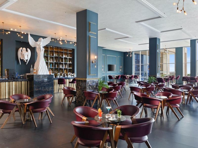 Modernes Restaurant mit runden Tischen, weinroten Stühlen und großen Fenstern für Tageslicht.